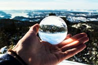 一只手持水晶球的户外特写，映出优美风景