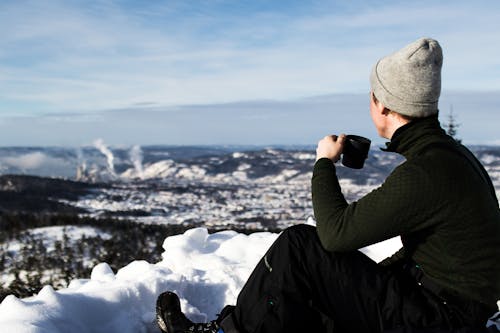 ジャケットを着て、雪の上に座ってカップを保持している男