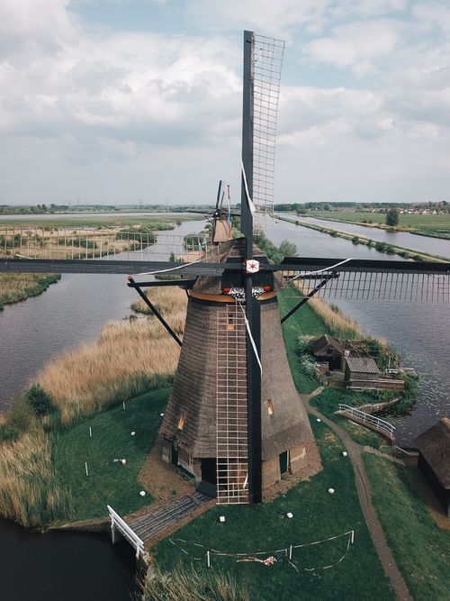 Free Stunning aerial view of a traditional Dutch windmill surrounded by rivers and lush fields under a cloudy sky. Stock Photo