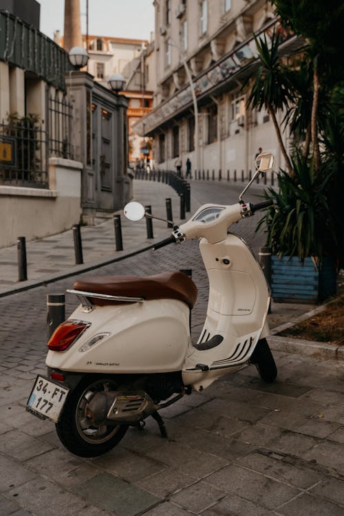 Free Retro fashioned scooter parked on narrow cobblestone street between aged historic buildings in city in sunny morning Stock Photo