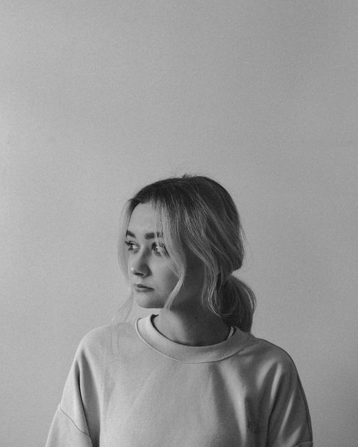 A black-and-white portrait of a young woman gazing thoughtfully sideways, creating a moody atmosphere.