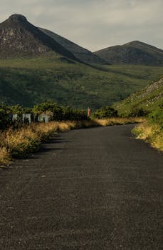 A tranquil road winds through a lush green valley with majestic mountains, ideal for nature lovers.