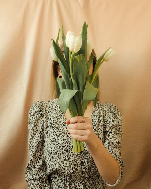 A woman in a leopard print dress holds white tulips, hiding her face, creating an artistic and mysterious vibe.