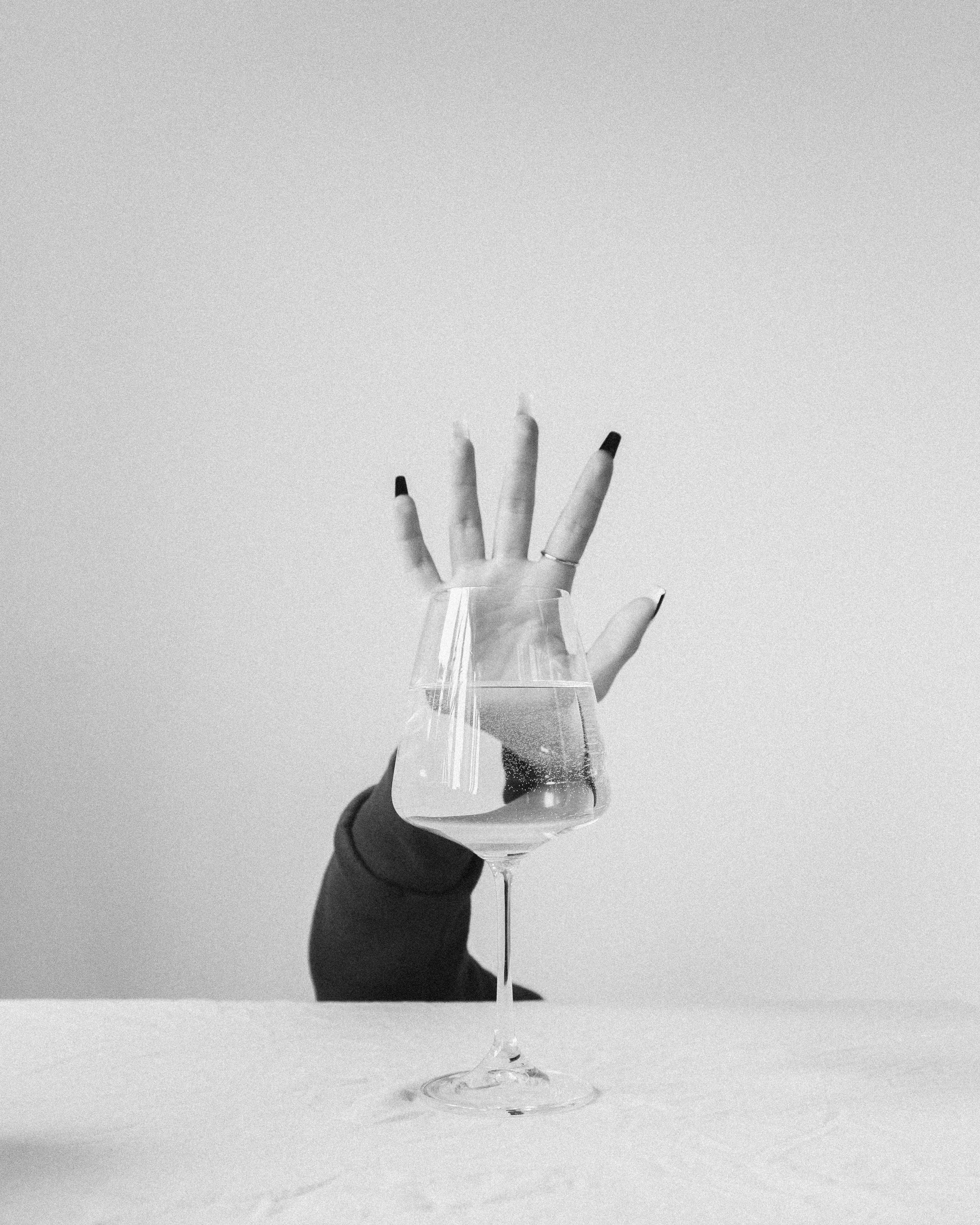 Black and white image of a hand behind a wine glass on a minimalist background.