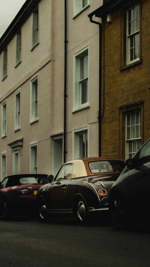 Free Classic Nissan Figaro parked on a quiet street against colorful building facades. Stock Photo