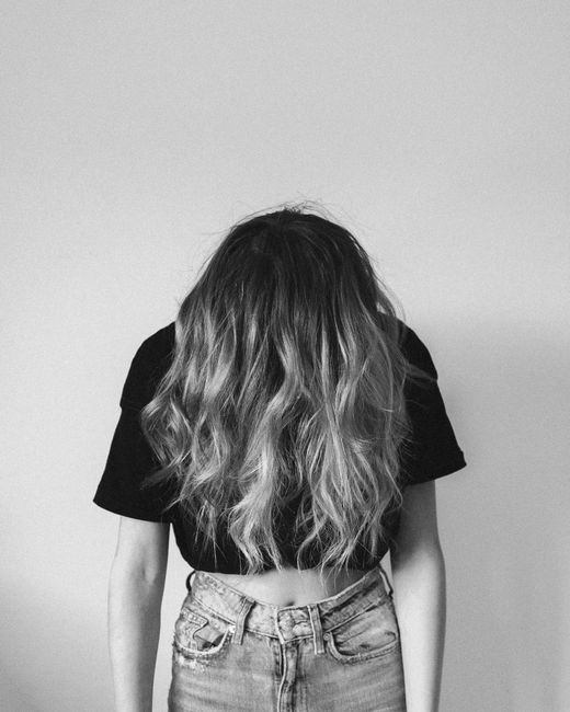 Monochrome portrait showcasing a woman in jeans with long wavy hair, head down.