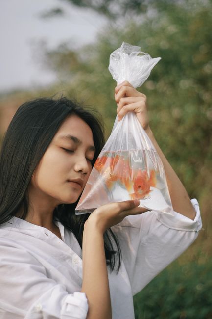 Peaceful woman with closed eyes holding a bag of goldfish in natural setting.