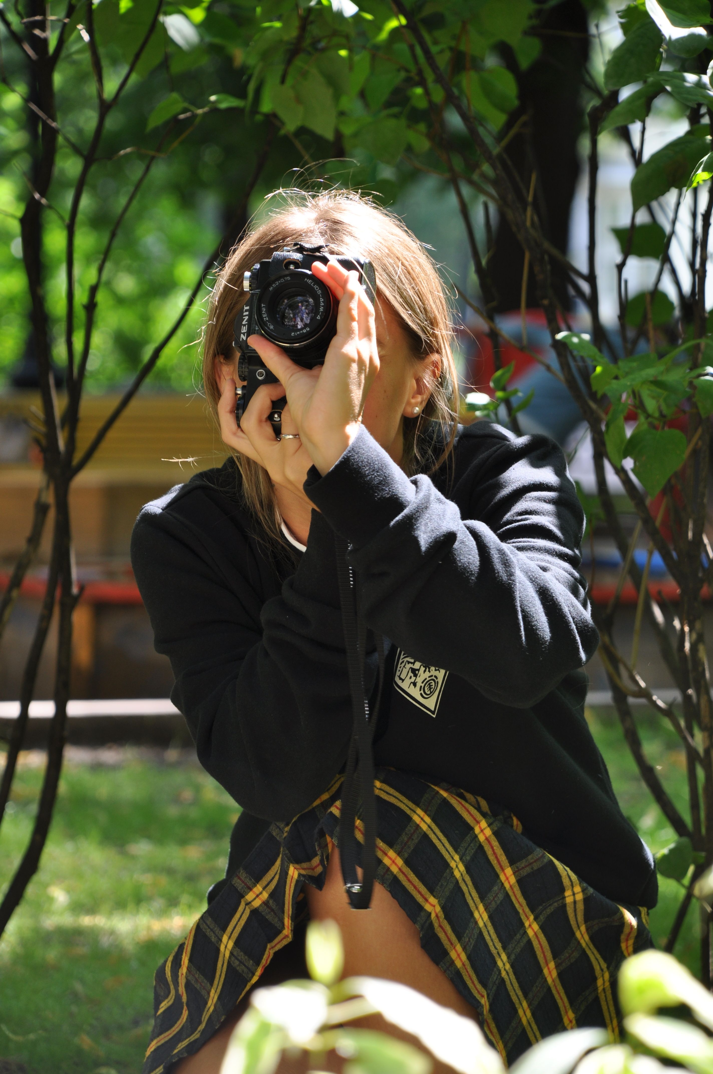 A young woman captures nature with a DSLR camera in a sunlit outdoor setting.