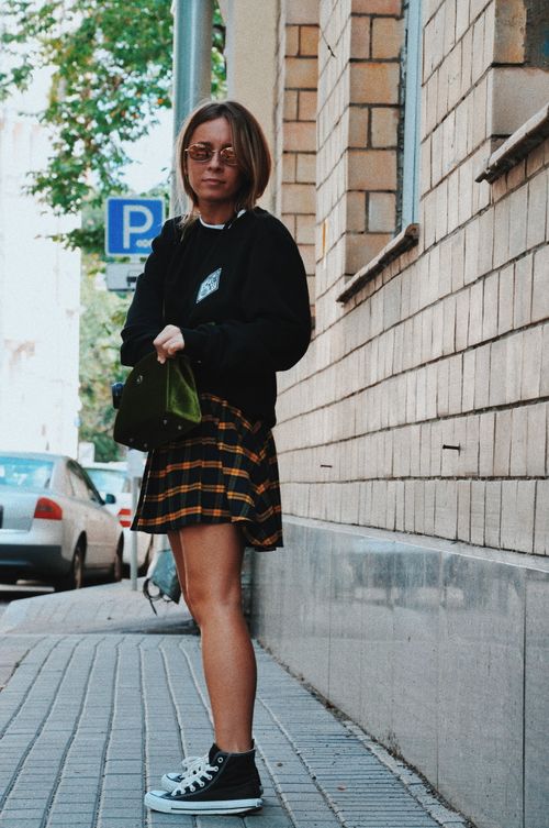 Free A woman in fashionable streetwear stands on city sidewalk wearing sunglasses and plaid skirt. Stock Photo