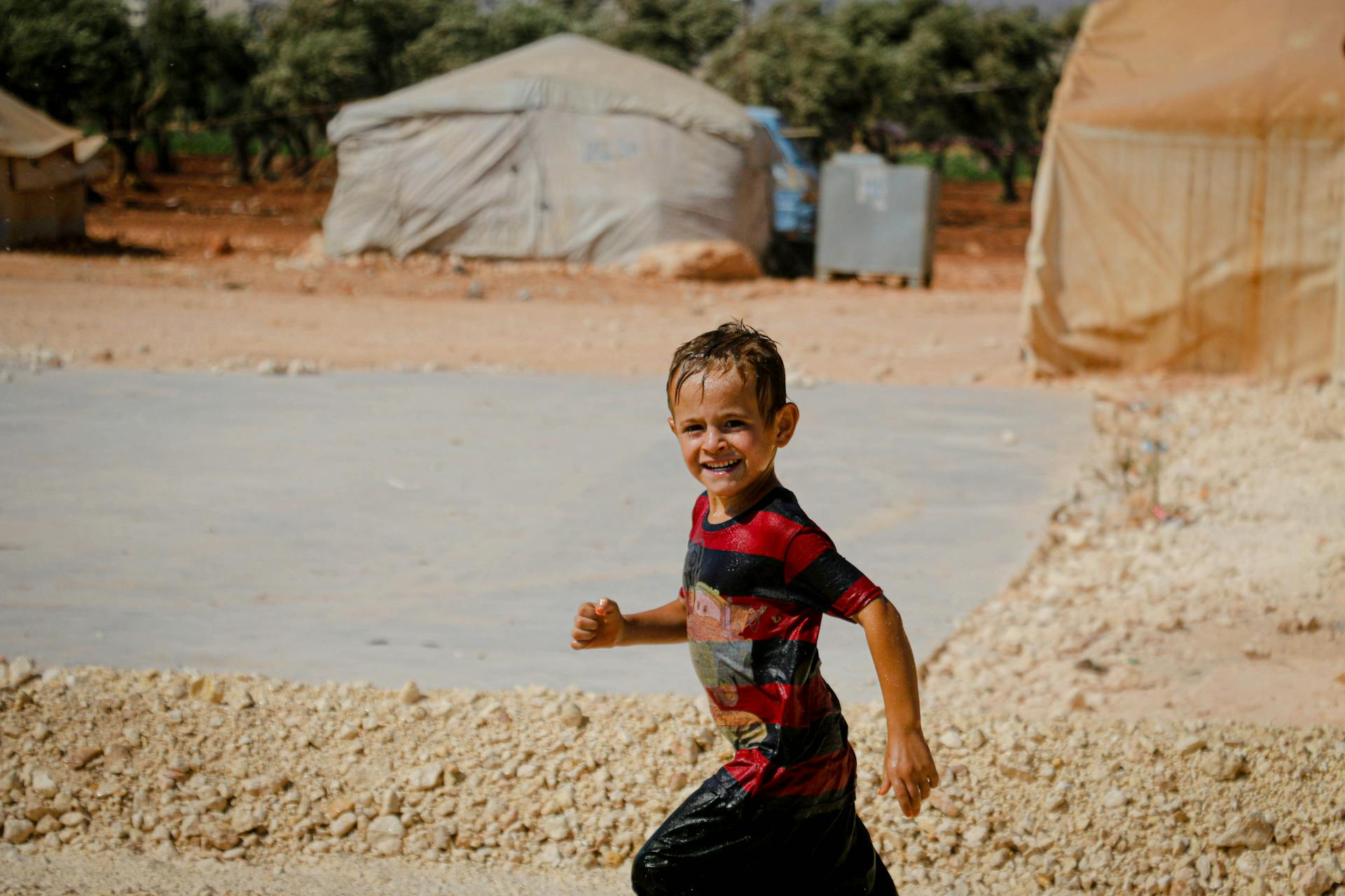 Smiling child running happily in a Syrian refugee camp under the sun, showcasing resilience and hope.