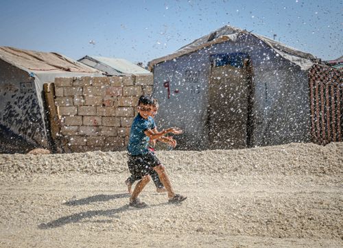 Free A young boy enjoying a playful moment with water in Idlib, Syria's refugee camp. Stock Photo