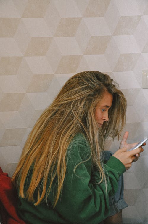 A Woman Wearing a Green Sweater Using Her Smartphone