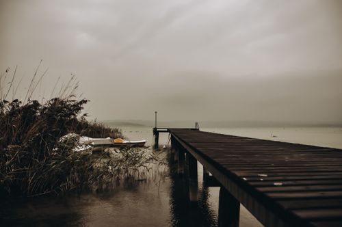 Free A serene lakeside pier surrounded by fog and docked boats, creating a moody atmosphere. Stock Photo