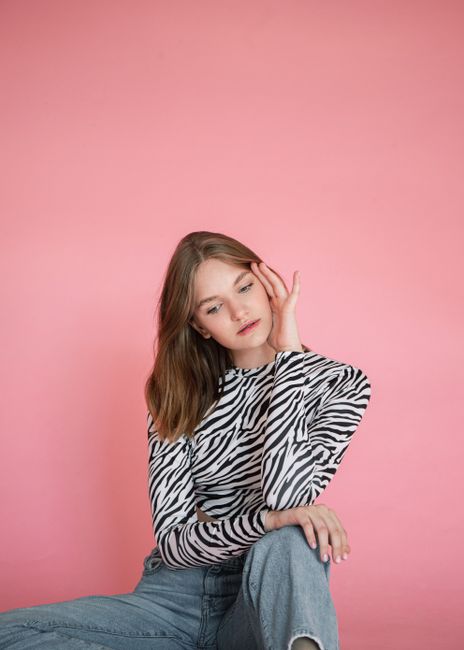 Stylish young woman posing in zebra print top with pink background, conveying a modern fashion vibe.