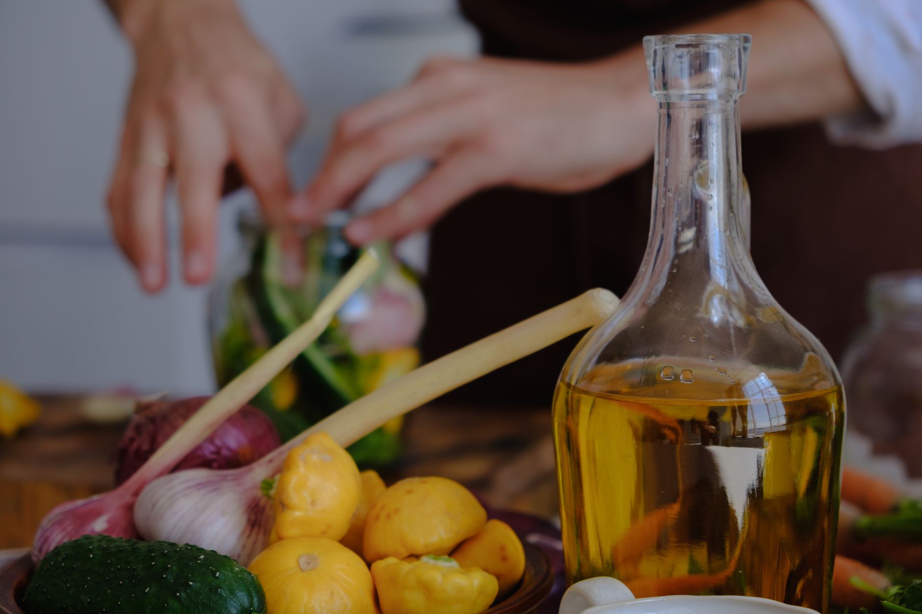 Hands preparing vegetables with olive oil, garlic, and squash in a kitchen setting.