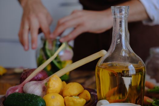 Hands preparing vegetables with olive oil, garlic, and squash in a kitchen setting.