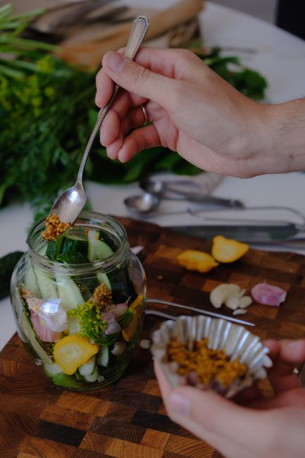A glass jar of dijon mustard with a small wooden spoon resting in it, surrounded by whole mustard seeds on a wooden table