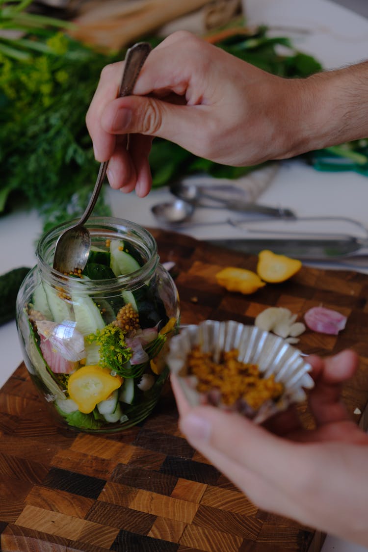 Person Putting Ingredients In A Glass Jar For Fermentation