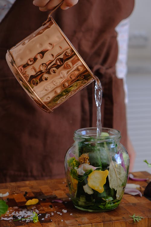 Person Pouring Water on Glass Jar With Green Leaves