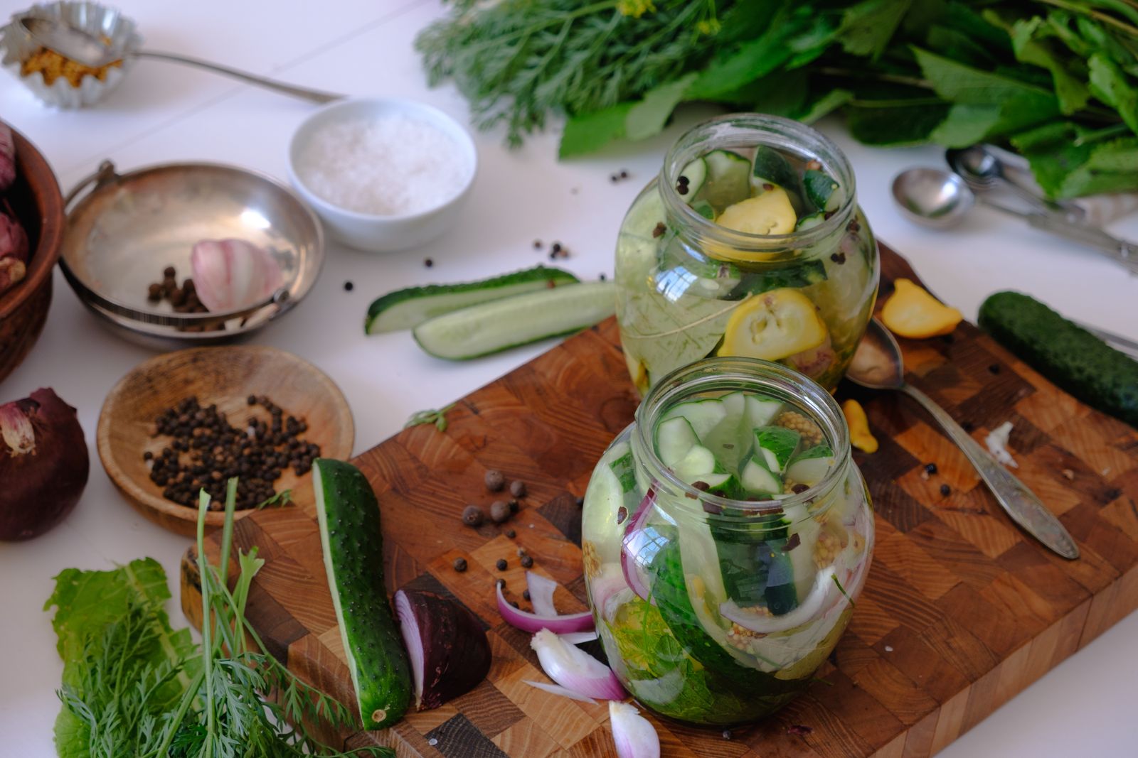 Jars of cucumber pickles on a board with herbs and spices