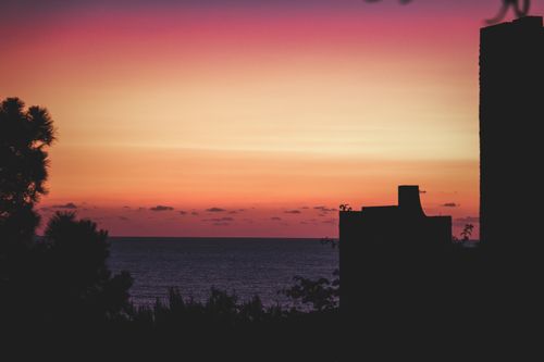 Free A stunning silhouette of a building against a vibrant ocean sunset. Stock Photo