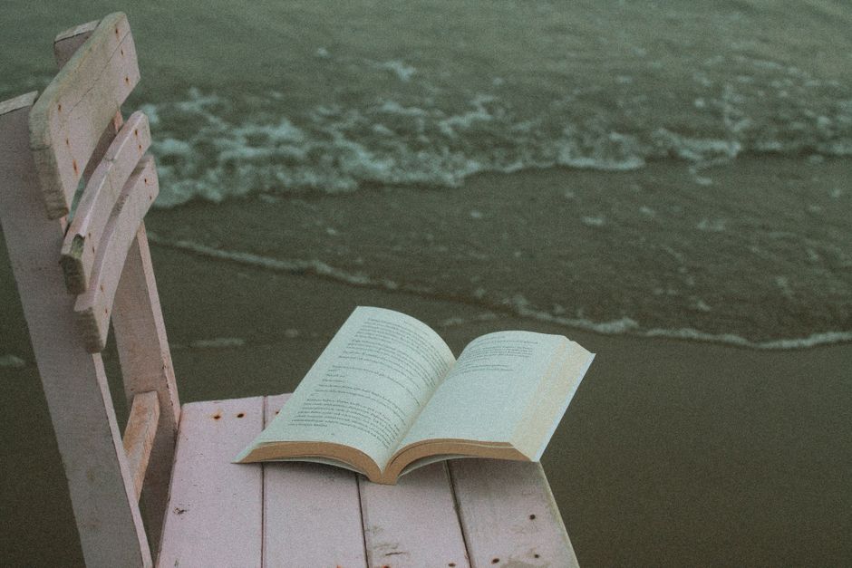 Open book on a wooden chair by the ocean at dusk, perfect for relaxation themes.