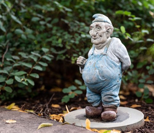 Free Whimsical garden gnome sculpture with a smiling face among green foliage, captured in a close-up outdoors. Stock Photo