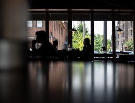 Silhouettes of people seen through glass, capturing urban dining scene.
