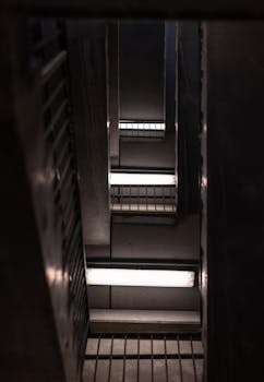 Vertical view of a multi-storey industrial staircase with fluorescent lighting.