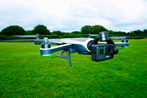 Free Close-up of a drone equipped with a camera flying over a vibrant green outdoor field. Stock Photo