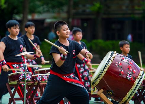 Energetic performance of Asian boys playing traditional Taiko drums outdoors in Taiwan.