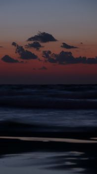 Calm ocean waves under a vibrant sunset sky with silhouetted clouds, creating a tranquil evening scene.