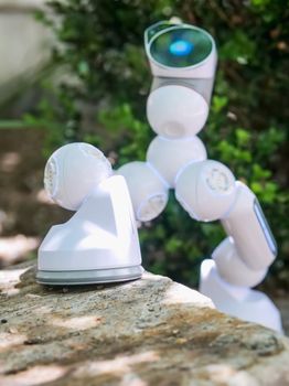 Close-up of a futuristic white robotic arm stepping over a rock outdoors.