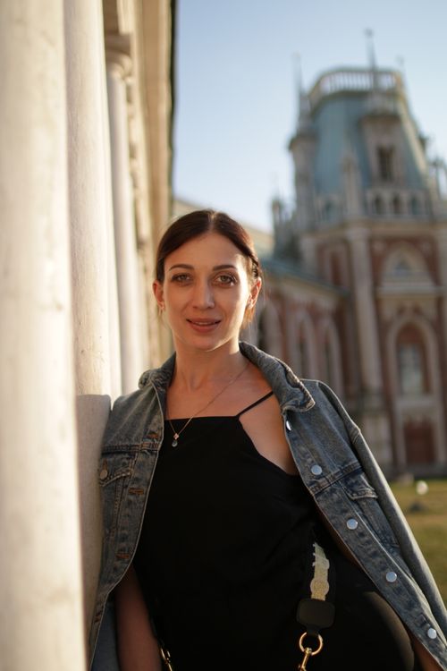 Free Caucasian woman in denim jacket posing outdoors near a historical building, smiling. Stock Photo