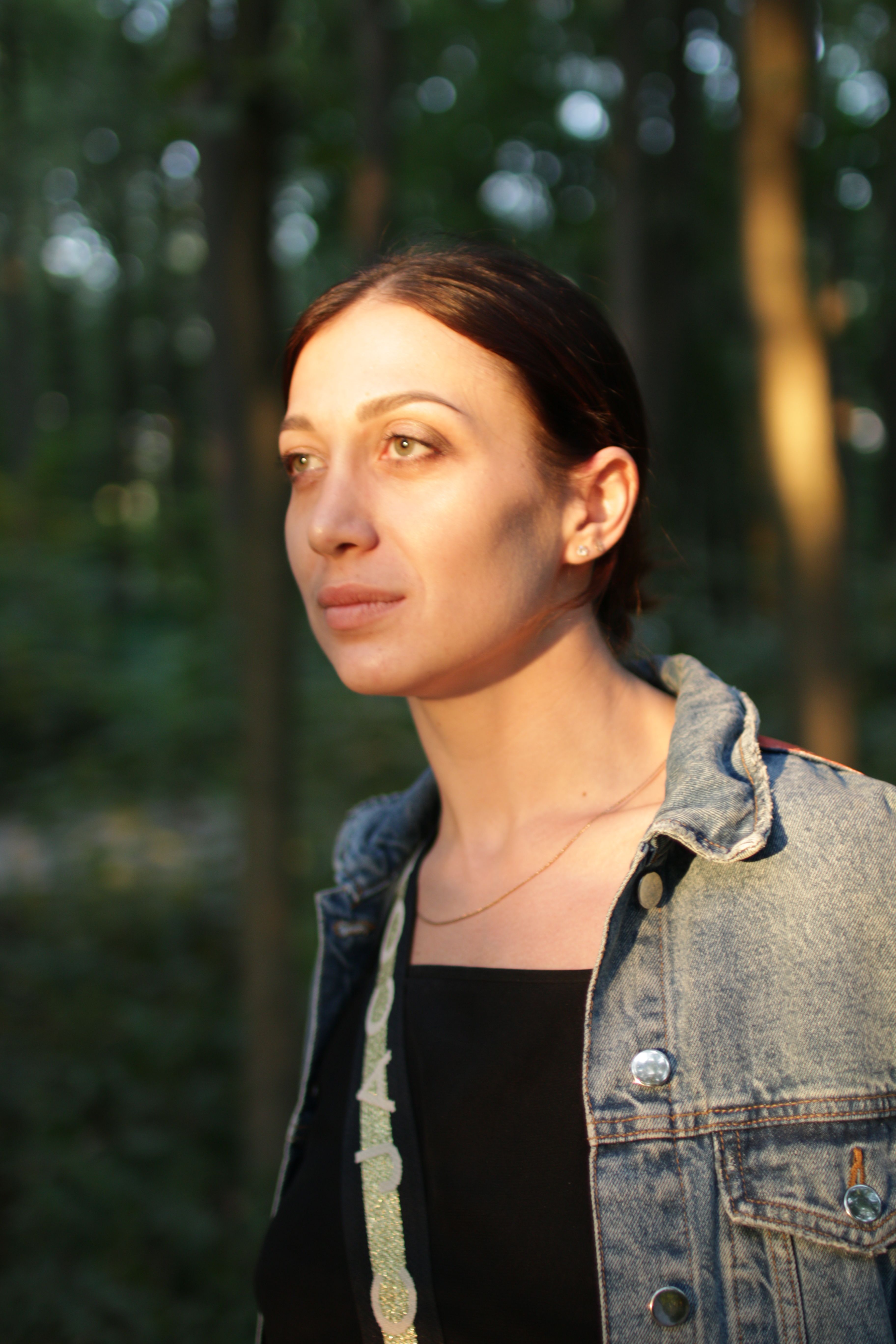 Portrait of a woman in a forest, wearing a denim jacket and illuminated by sunlight.