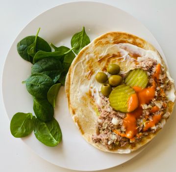 Delicious tuna wrap with pickles and a side of spinach, perfect for a tasty meal.