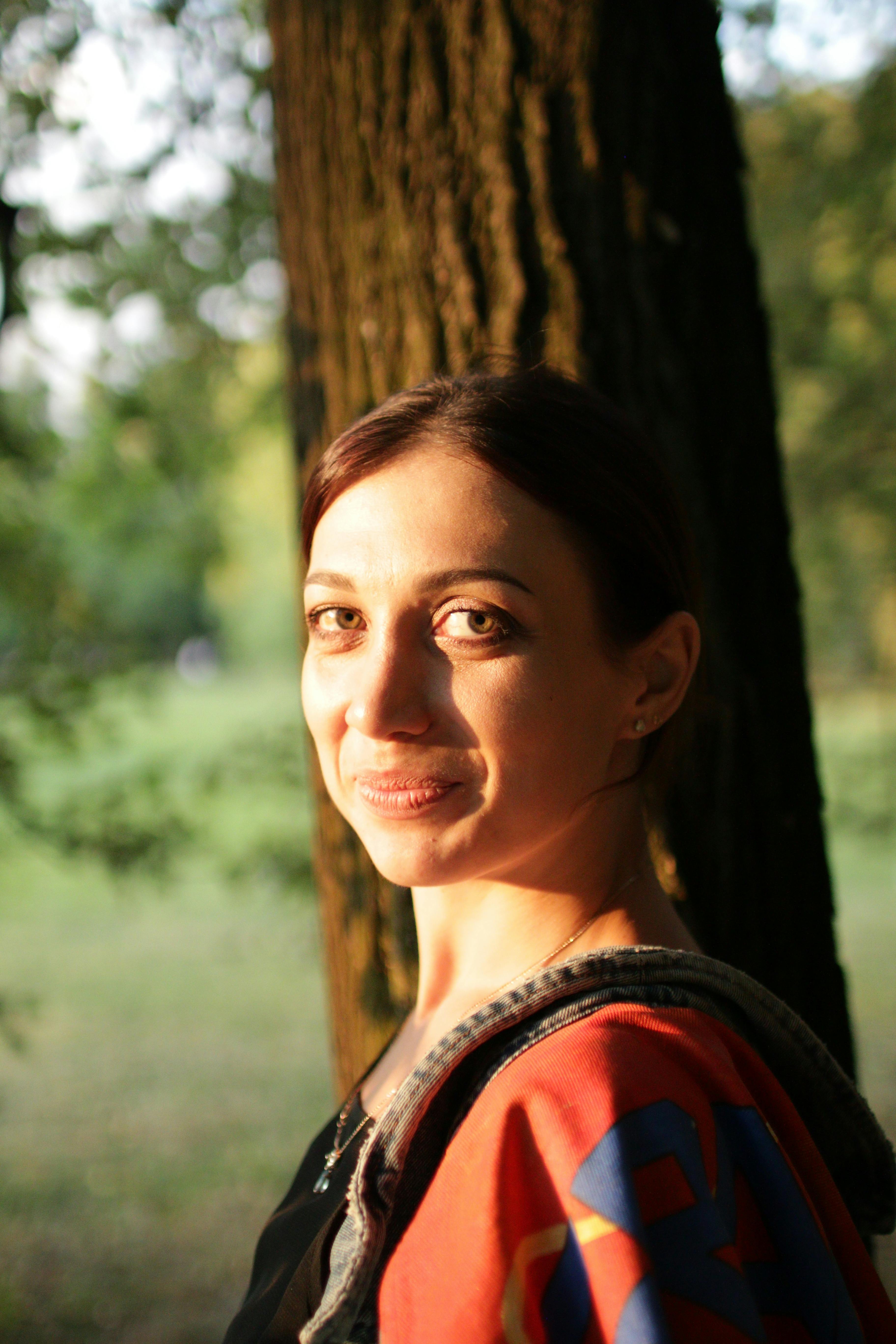 A woman smiling in a sunlit forest, capturing a serene outdoor moment.