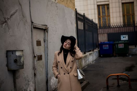 Woman in Beige Coat Wearing Black Hat Standing Beside White Wall