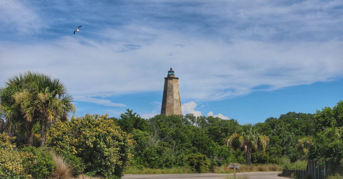 View of Old Baldy Lighthouse surrounded by greenery under a vivid blue sky in North Carolina.