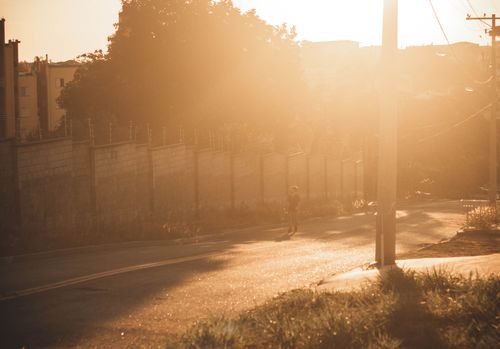 Free A person walking down a sunny road during golden hour, casting long shadows in the warm glow. Stock Photo