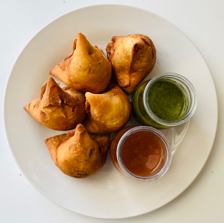 Crisp samosas served with green and tamarind chutney, seen from above