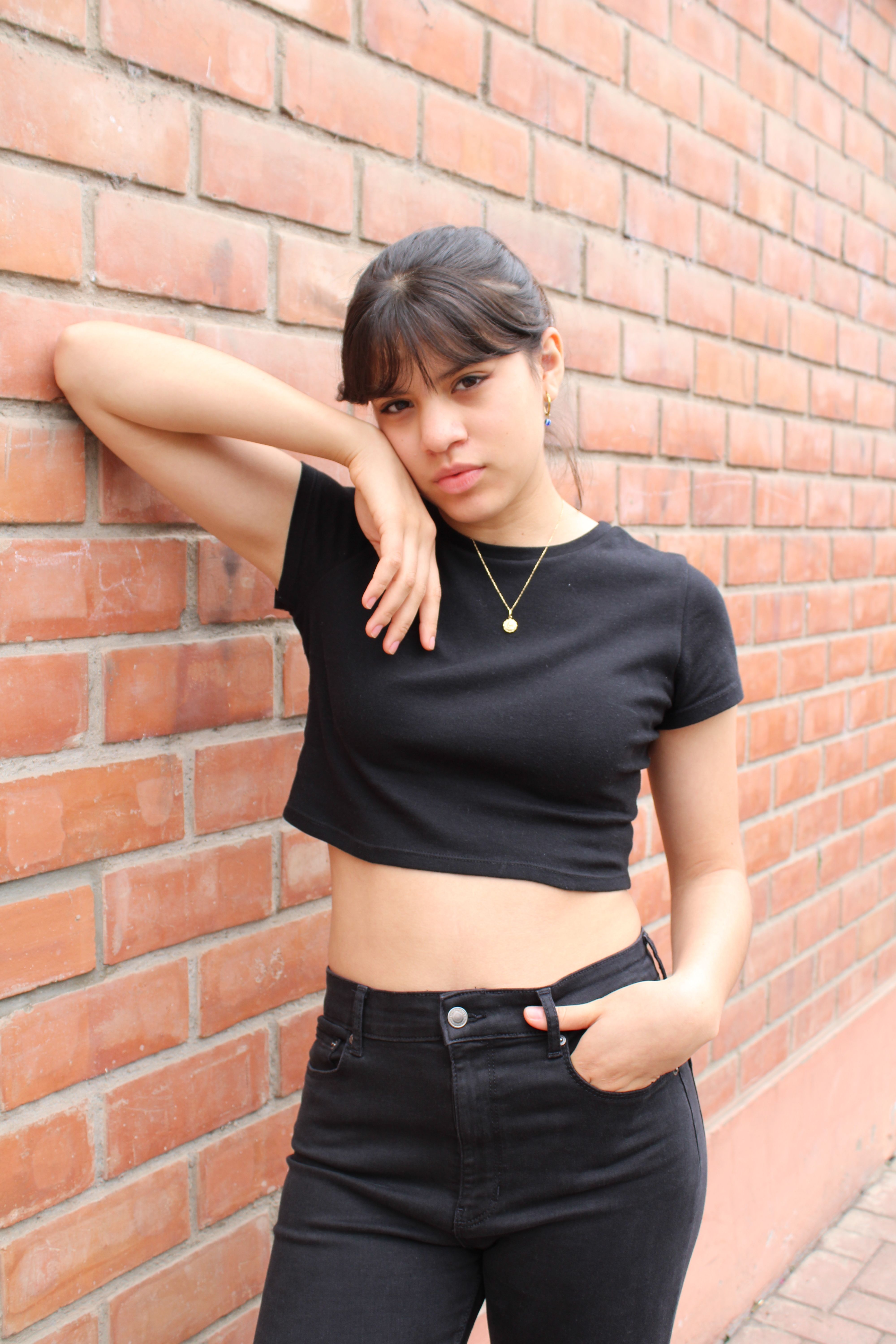 Casual portrait of a woman posing in black attire leaning on a brick wall.