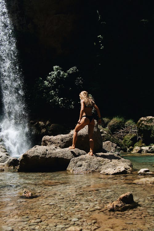 Woman in Black Bikini Standing on Rock Near Waterfalls