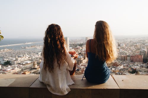 Free Two Young Women Sitting on Bench and Looking at the City From Above Stock Photo