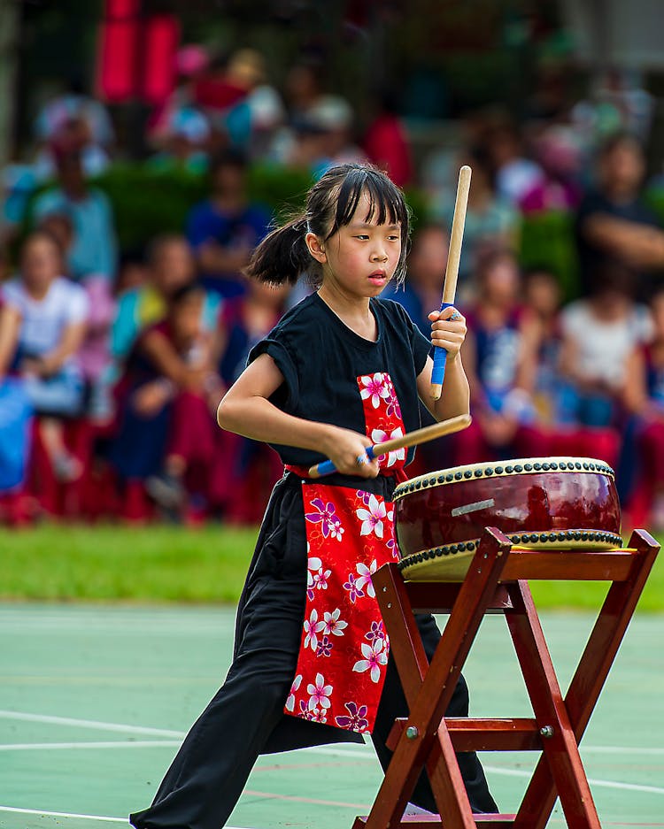 Girl In Black Clothes And Red Apron Playing Drum