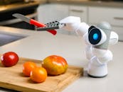 A Clicbot Holding a Knife Beside a Wooden Chopping Board with Tomatoes