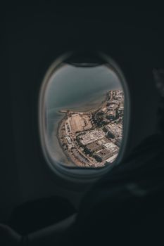 Breathtaking aerial view of coastline and city through airplane window, showcasing urban and natural landscapes.