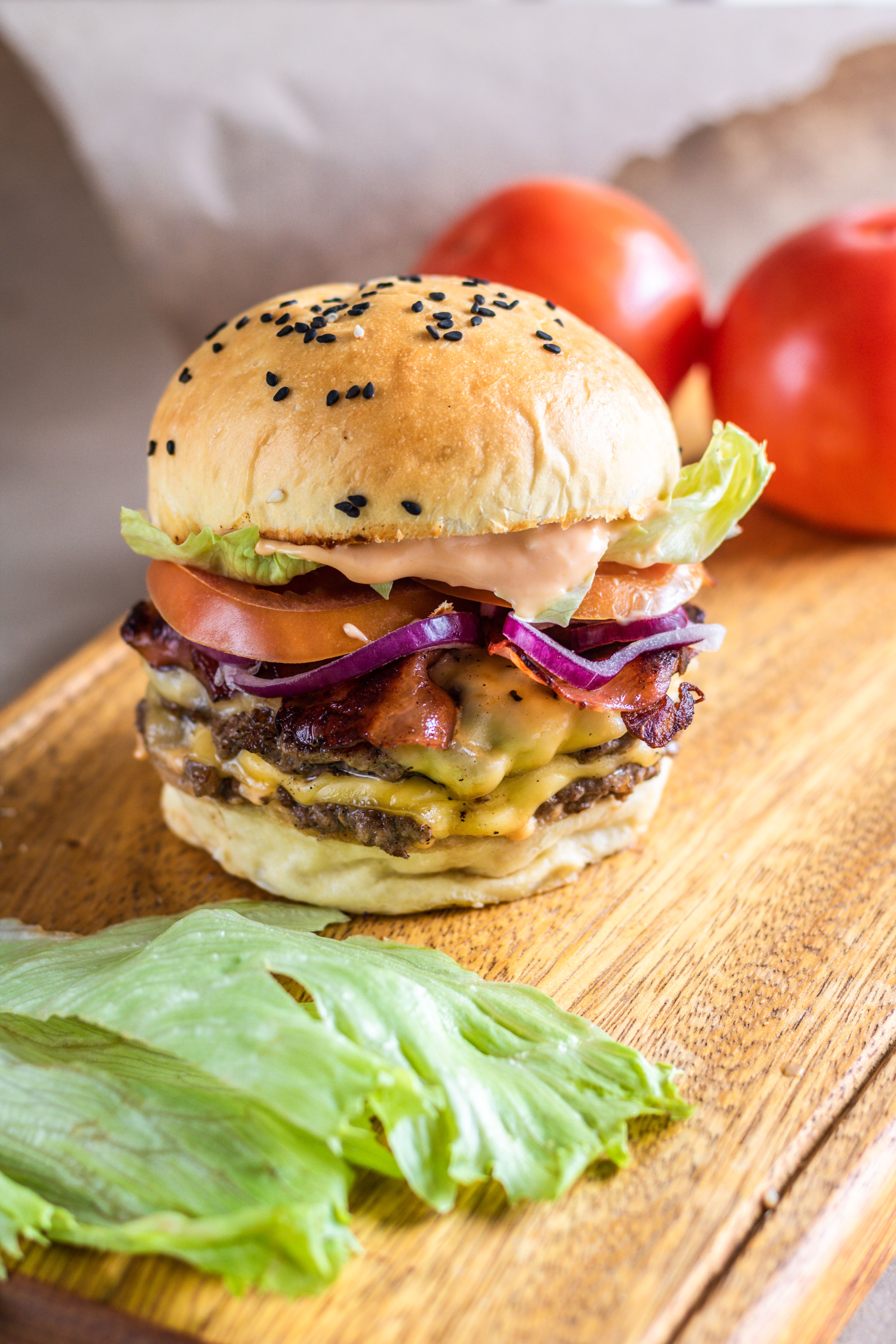 Mouthwatering cheeseburger with bacon, lettuce, and tomato served on a wooden board.