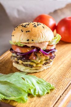Mouthwatering cheeseburger with bacon, lettuce, and tomato served on a wooden board.
