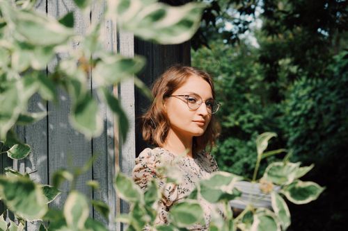 Free A serene portrait of a woman with glasses, surrounded by lush greenery in a garden setting. Stock Photo